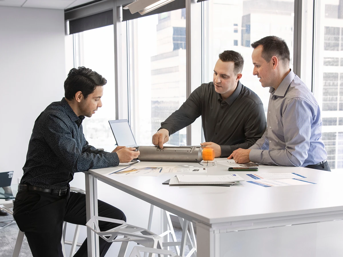 Three men are engaged in a discussion around a table in an office.