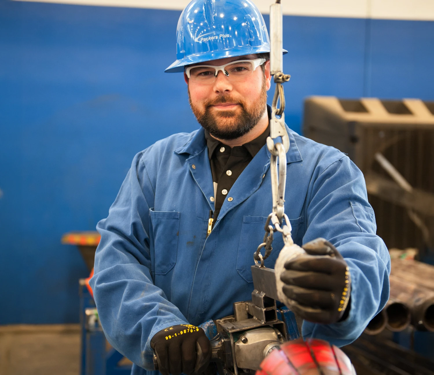 A Packers Plus employee wearing a blue hard hat, safety glasses, and a blue uniform operates industrial equipment.