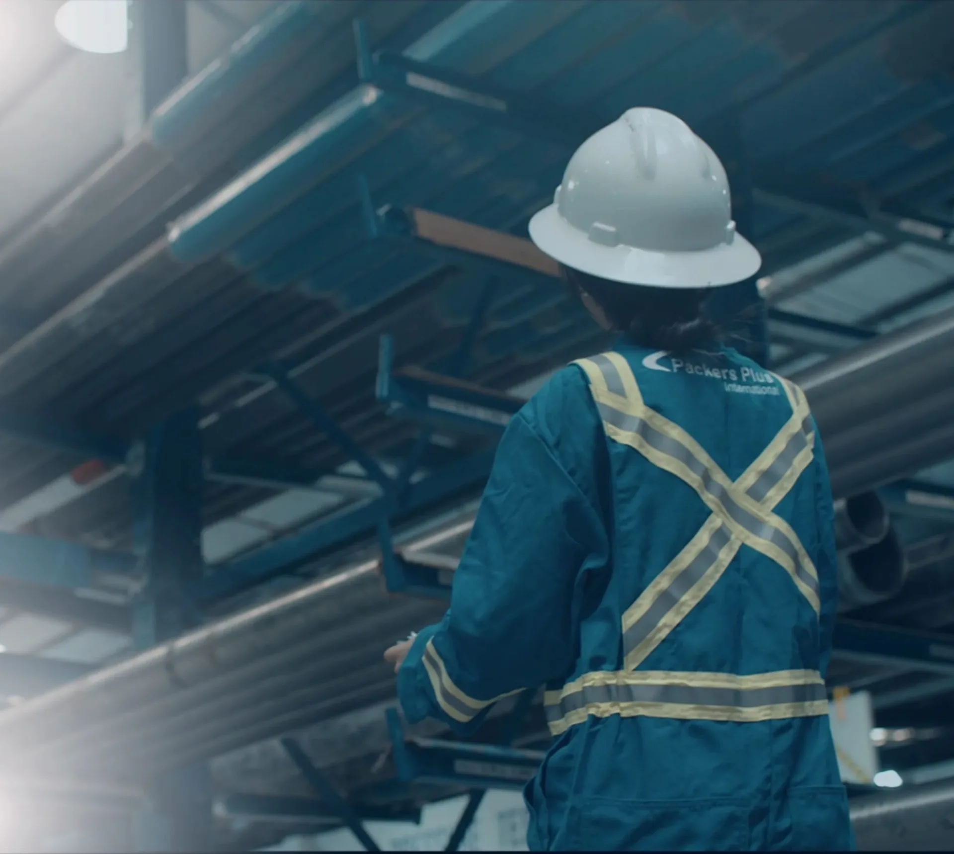 A Packers Plus worker in safety gear inspecting steel beams in an industrial construction site.